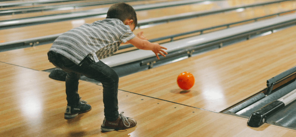 little kid rolling a bowling ball down the bowling lane